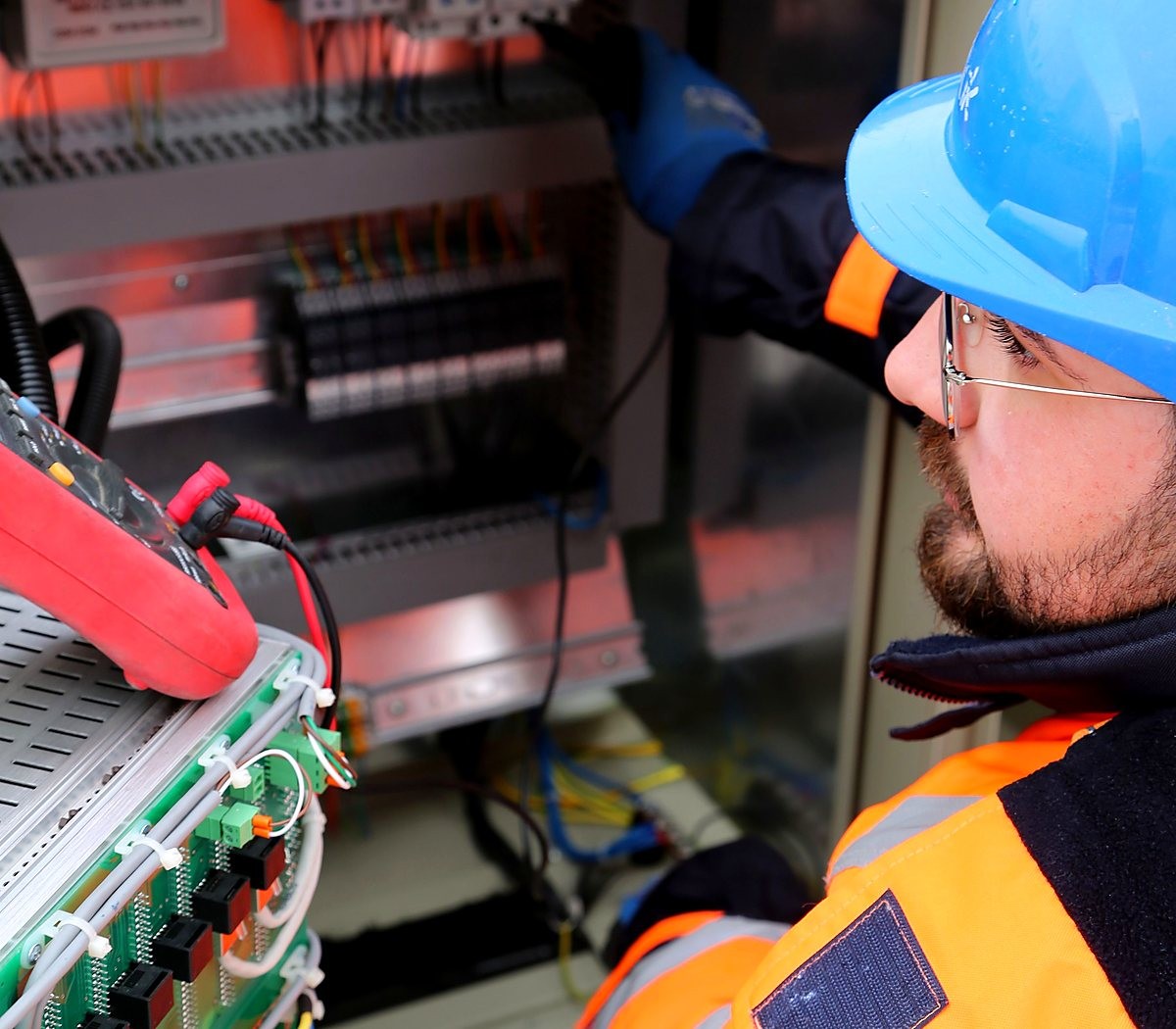 Técnico com capacete testando um painel eletrônico com multímetro